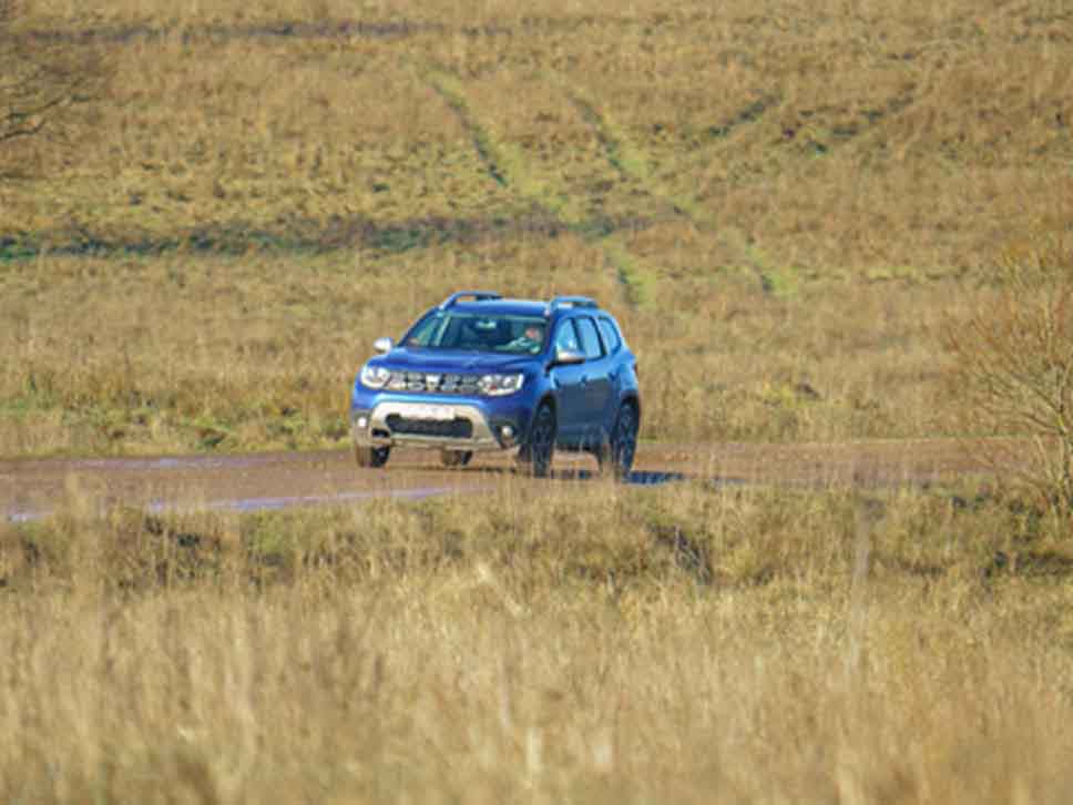 Dacia Duster driving along a dirt track in the middle of a field