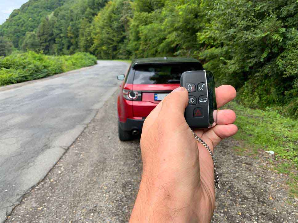 Hand using remote car key to open Land Rover Discovery